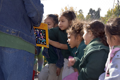Elementary school teacher and students outside looking at book Elementary school teacher and students outside looking at book