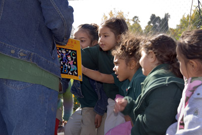 Elementary school teacher and students outside looking at book